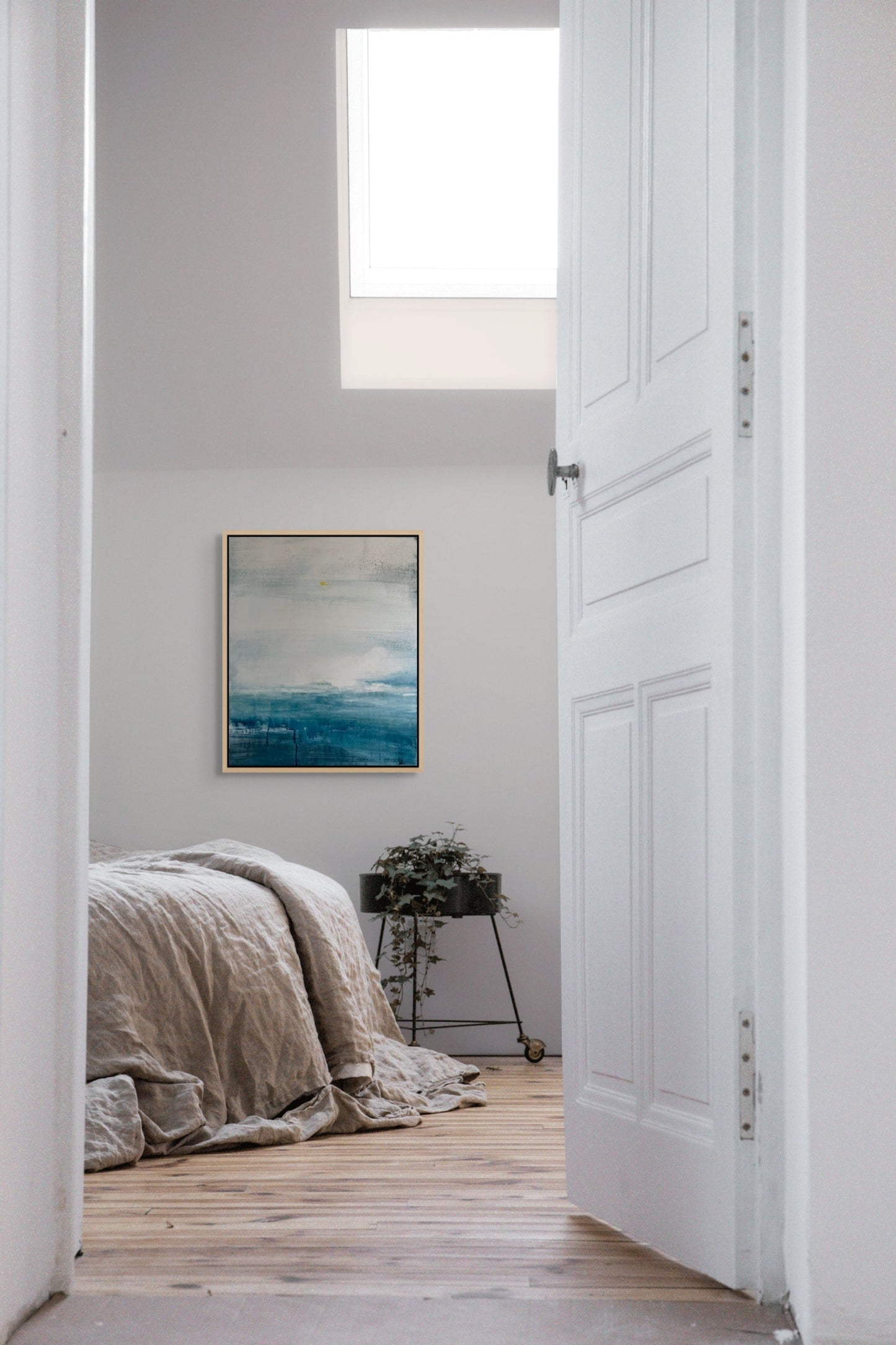 Bedroom with a bed, plant, and abstract seascape painting on a white wall.