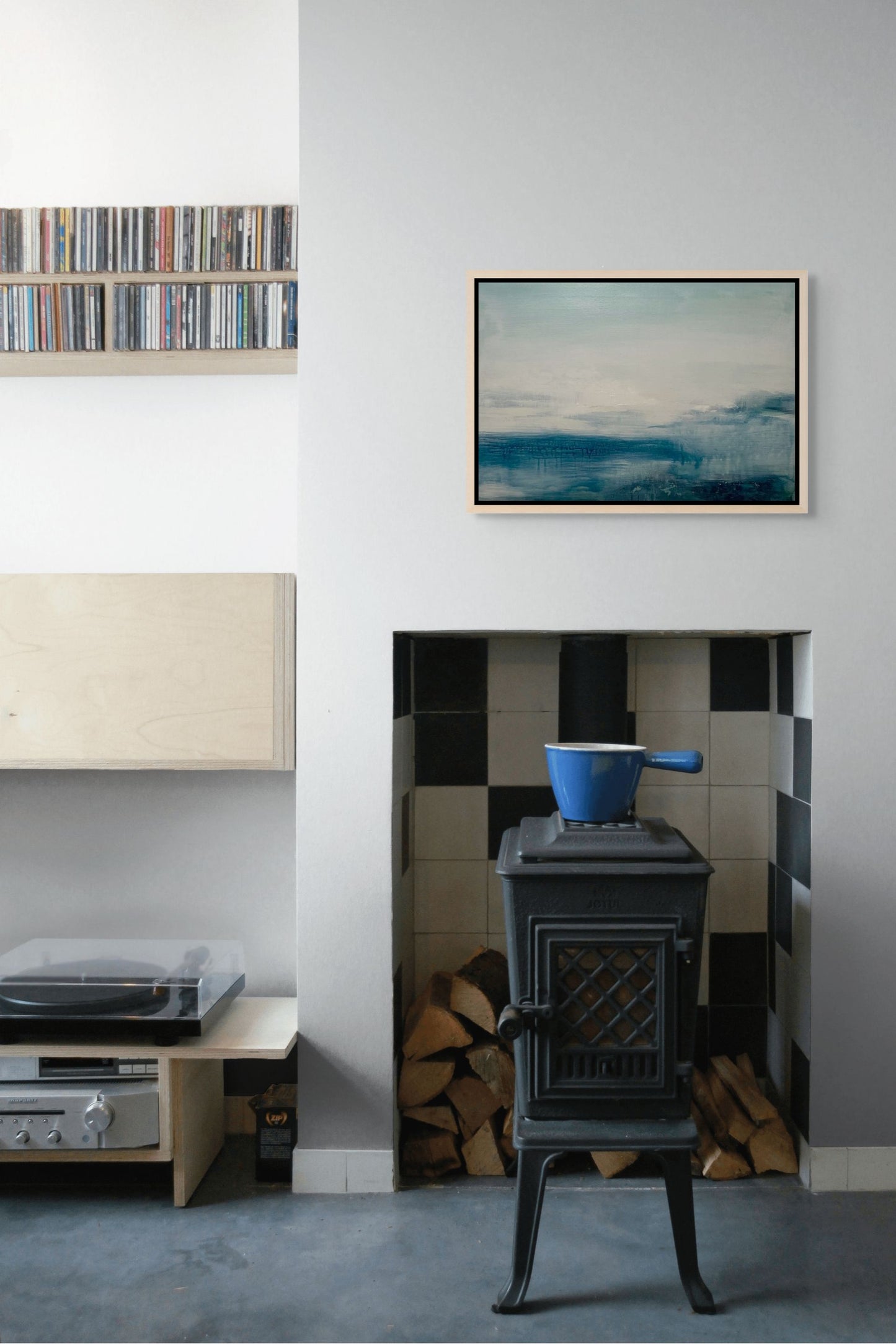 Small stove with a blue pot inside a room with a shelf, blue abstract seascape artwork, and record player.