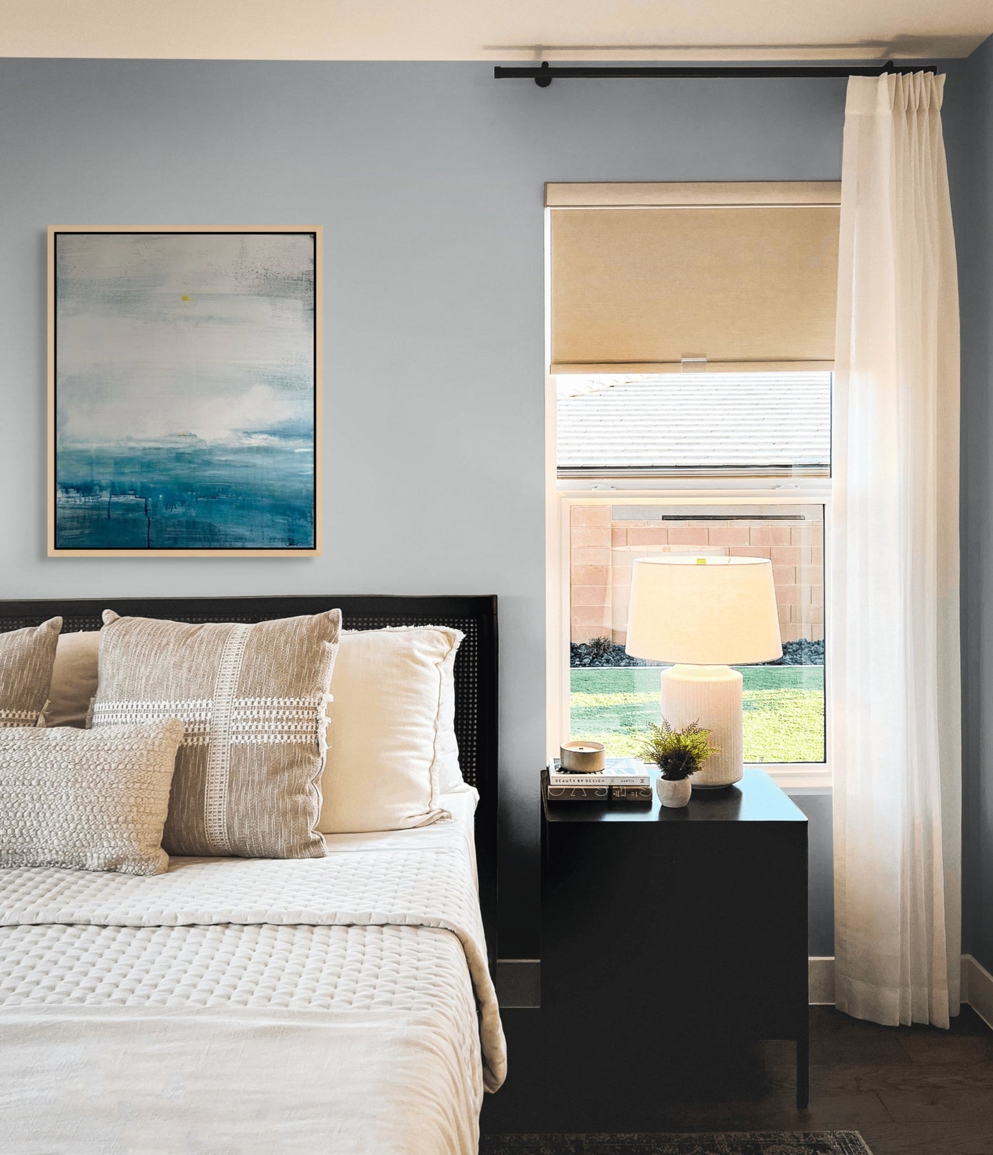 Modern bedroom with a bed, nightstand, lamp, and abstract seascape artwork on a grey wall.