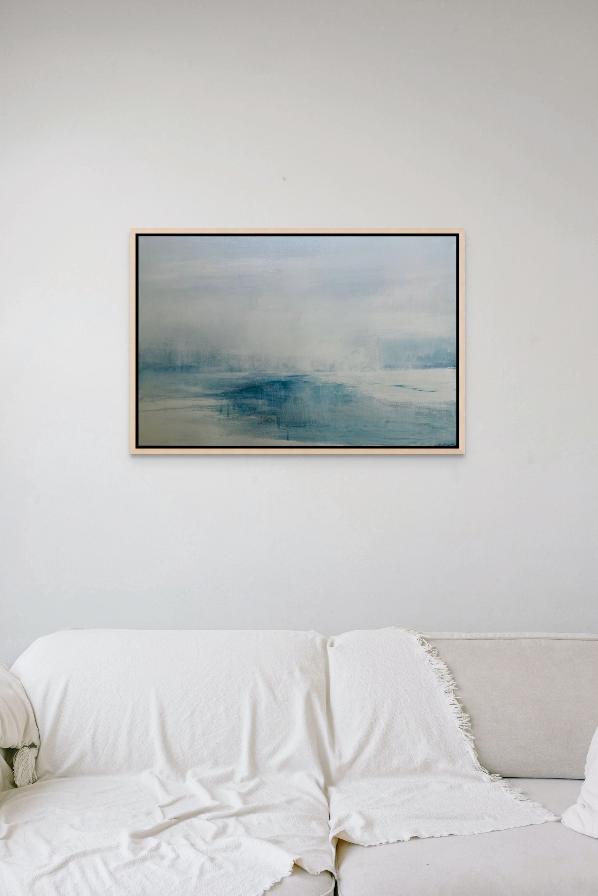 Framed abstract sea blue artwork on a white wall above a white sofa.