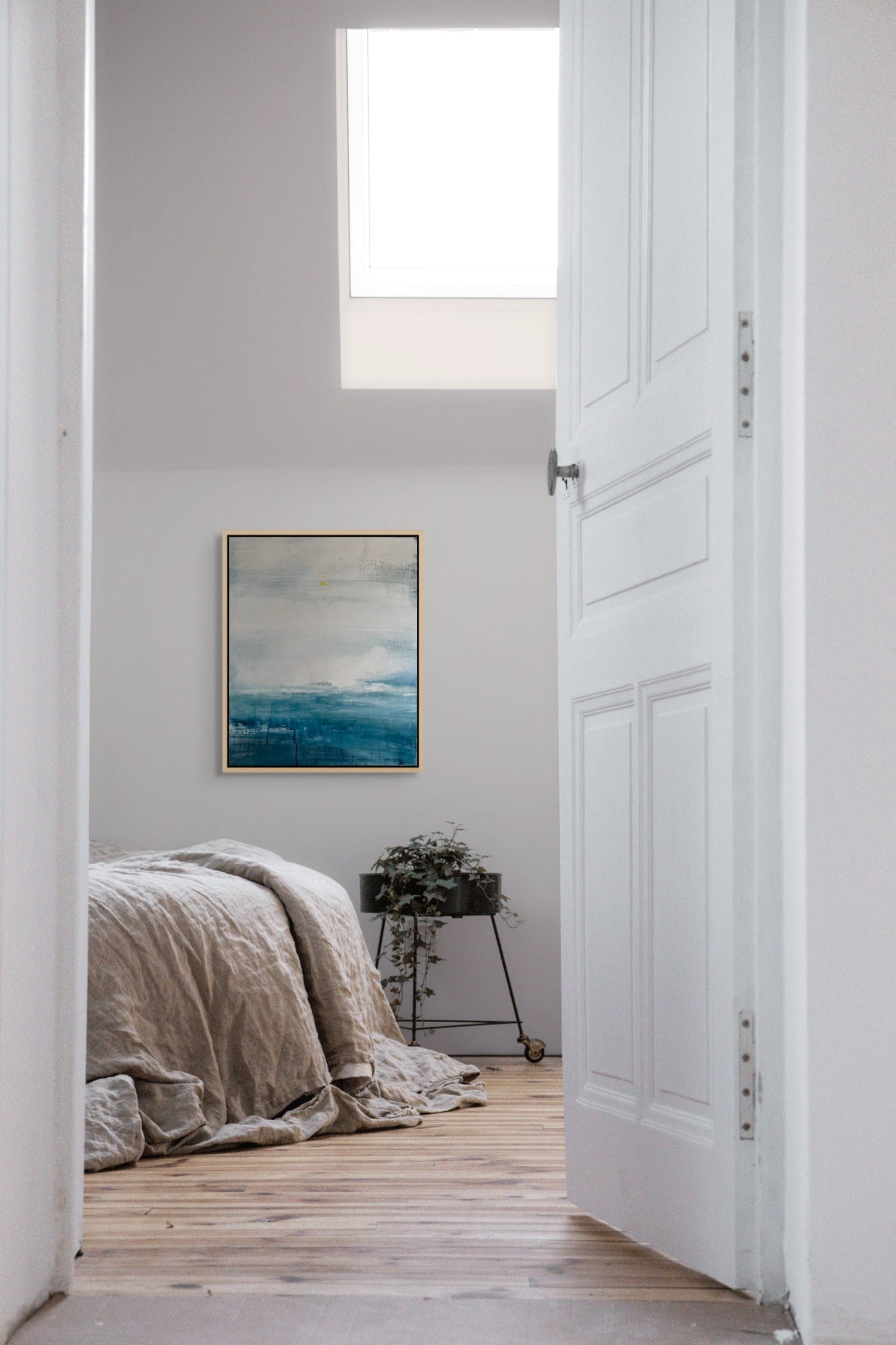 Bedroom with a bed, plant, and abstract seascape painting on a white wall.