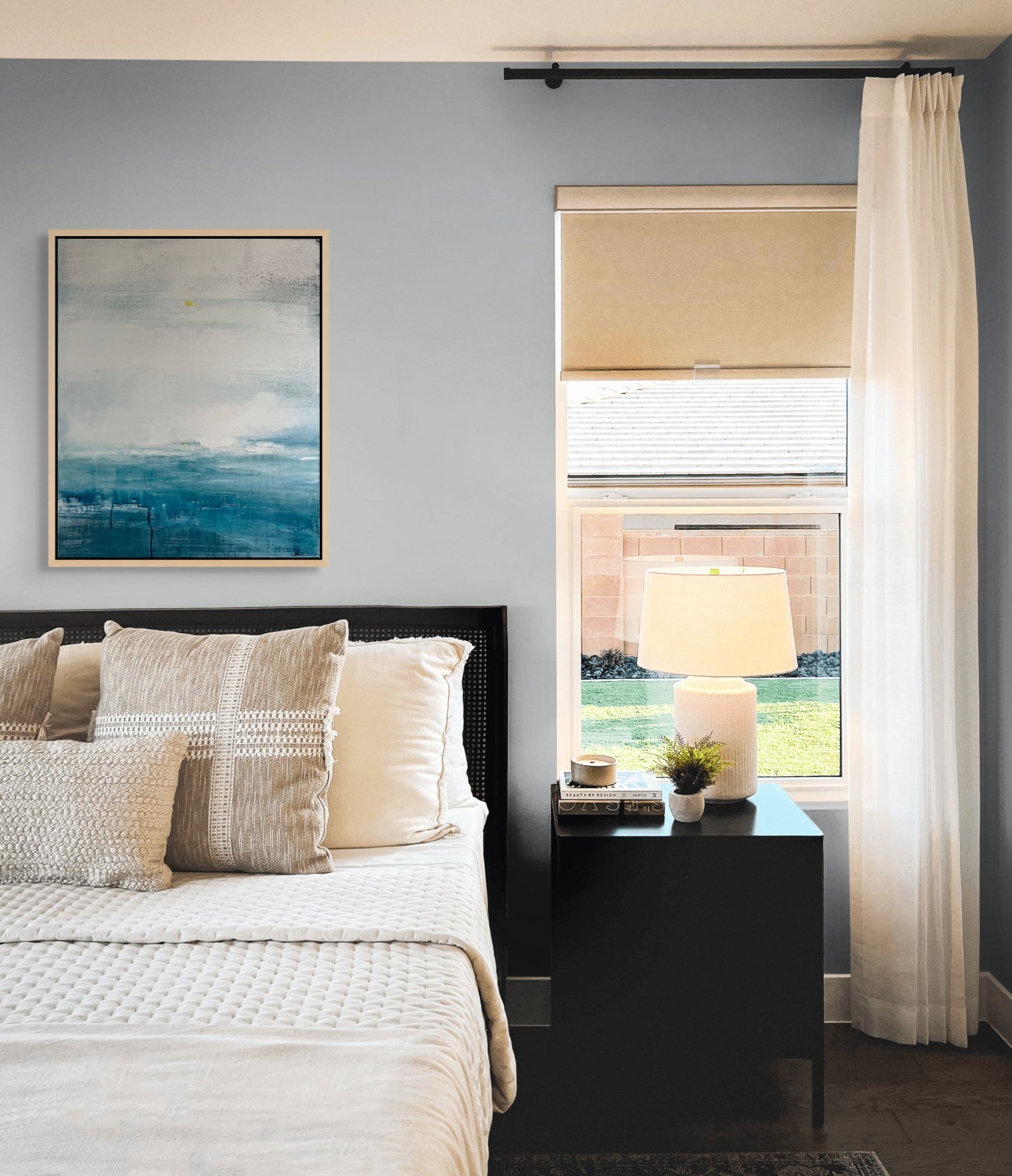 Modern bedroom with a bed, nightstand, lamp, and abstract seascape artwork on a grey wall.